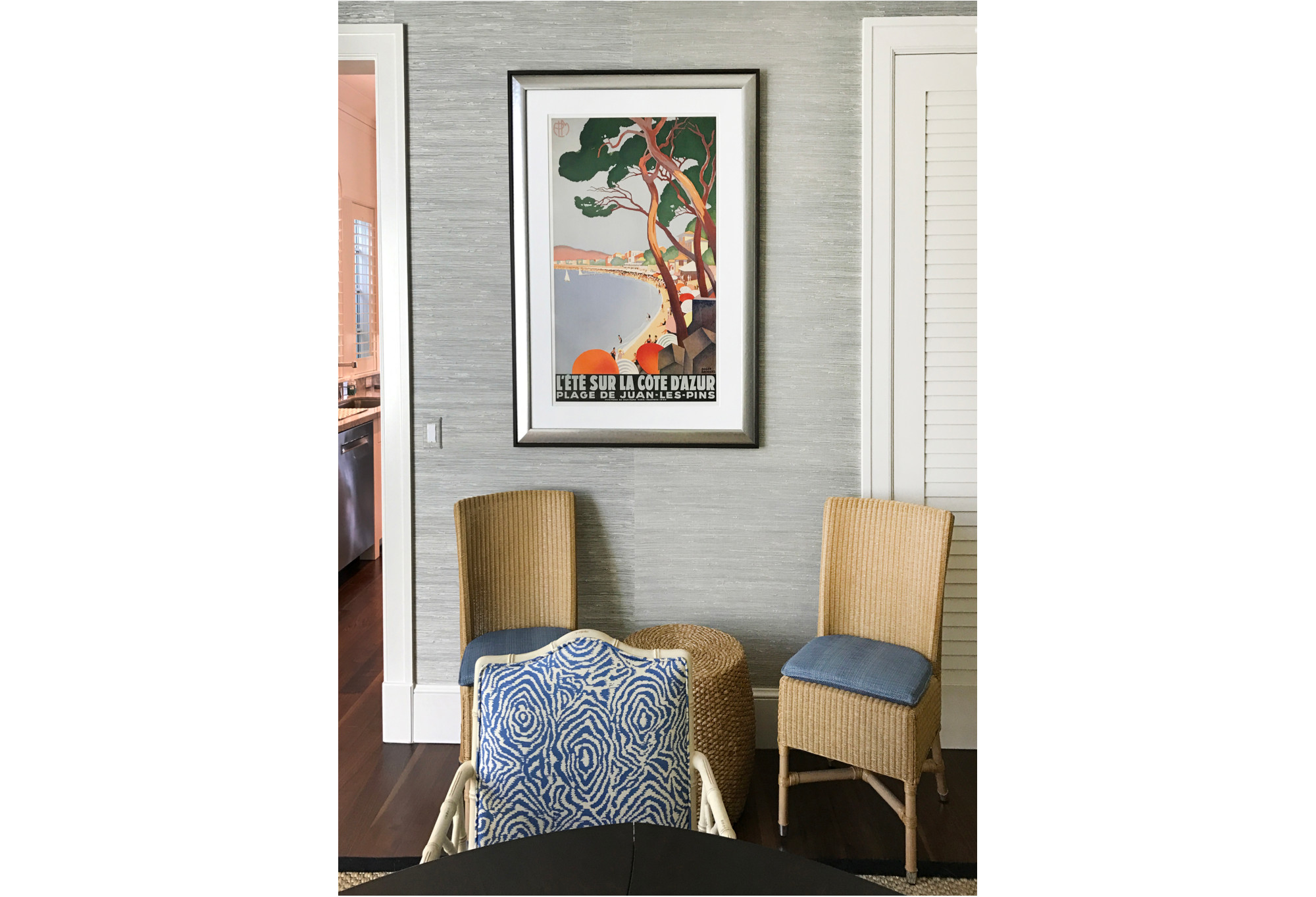 framed beach scene poster on wall with wicker chairs; blue, orange, tan, black, gray