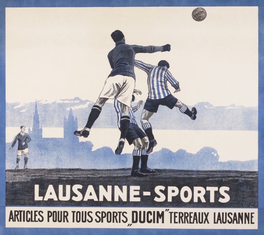 Soccer layers with Goalie punching the ball clear with lausanne cathedral and Lake behind; blue, white, black